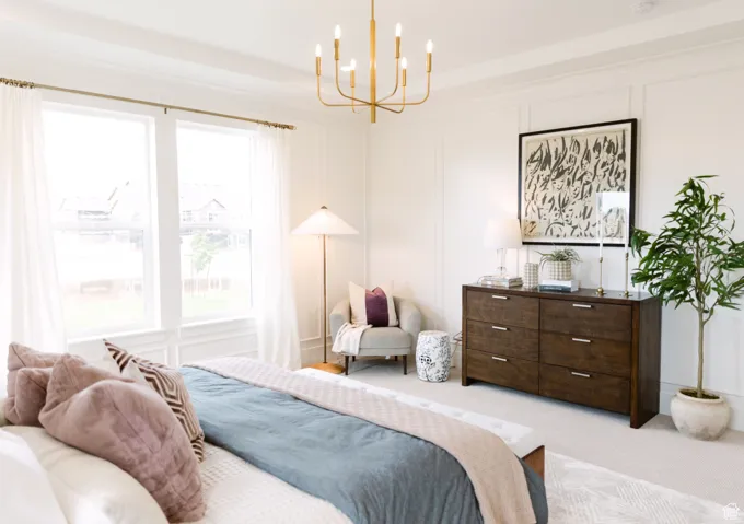 Bedroom with light colored carpet, a chandelier, and multiple windows