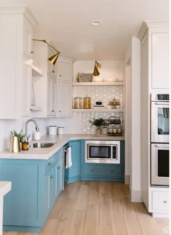 Kitchen with sink, appliances with stainless steel finishes, tasteful backsplash, blue cabinets, and light wood-type flooring