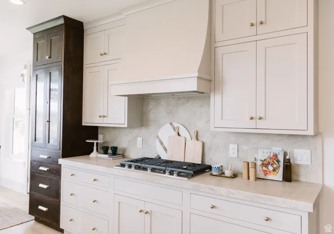 Kitchen with custom exhaust hood, tasteful backsplash, white cabinets, and stainless steel gas stovetop