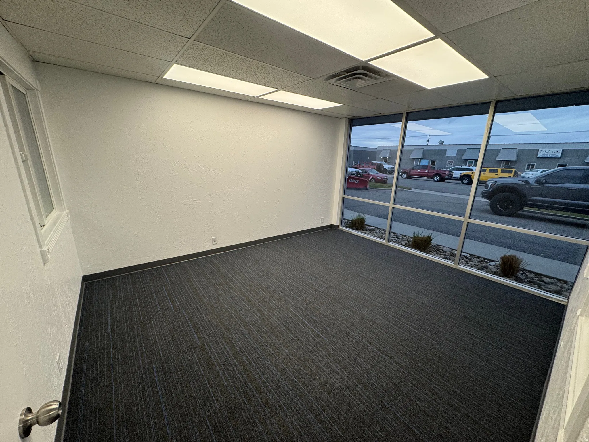 Carpeted empty room featuring a textured wall, floor to ceiling windows, and a drop ceiling