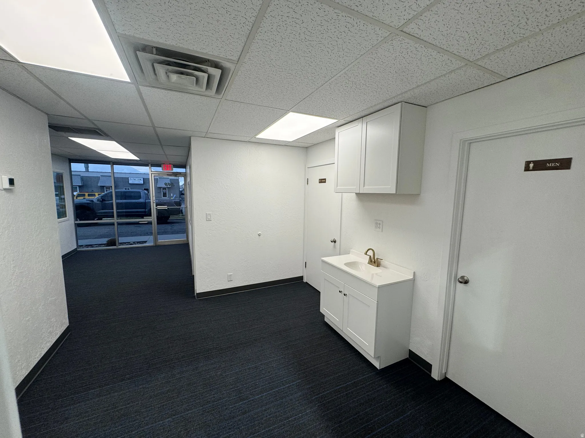 Corridor with a drop ceiling, dark carpet, and a textured wall