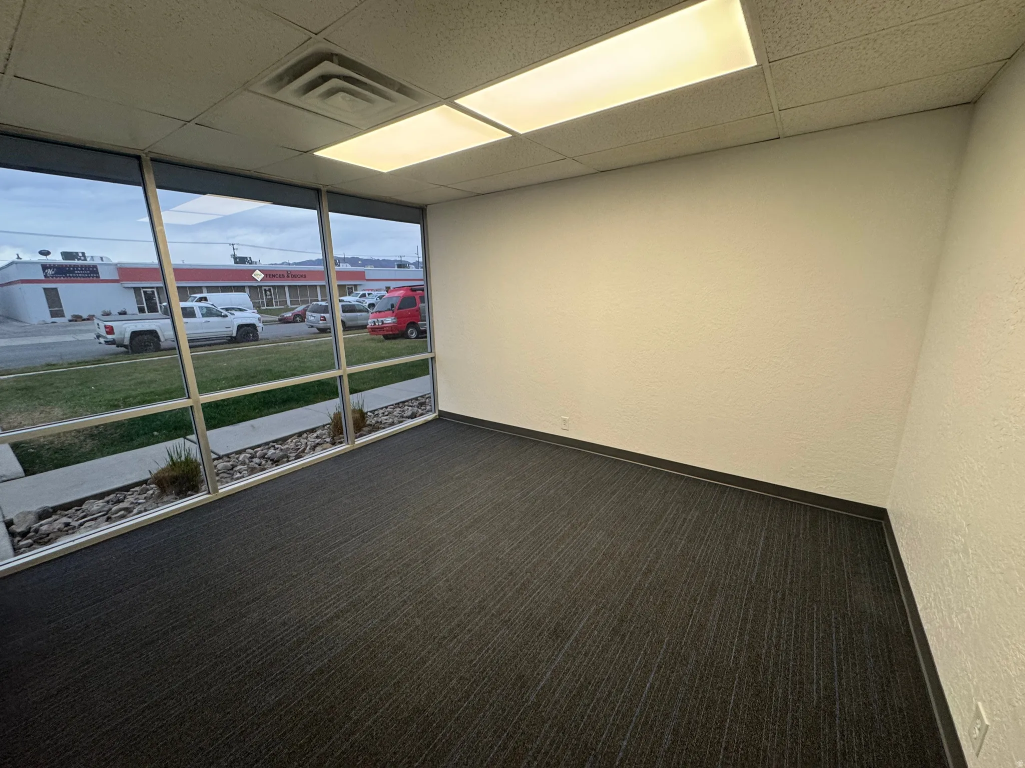 Spare room featuring a wall of windows, carpet, a paneled ceiling, and a textured wall