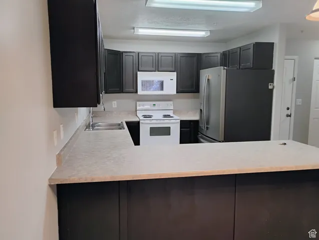 Kitchen featuring light countertops, a sink, a peninsula, and white appliances