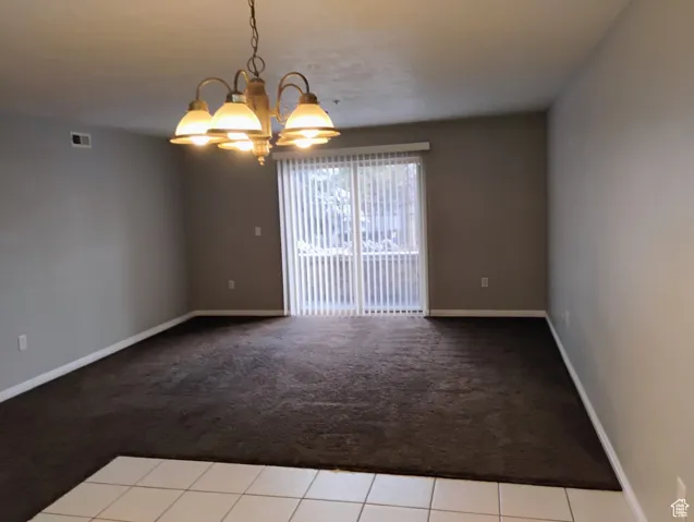Carpeted empty room with baseboards, a notable chandelier, visible vents, and tile patterned floors