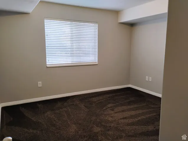 Empty room featuring baseboards and dark carpet