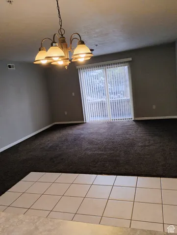 Tiled spare room with carpet floors, baseboards, a chandelier, and visible vents