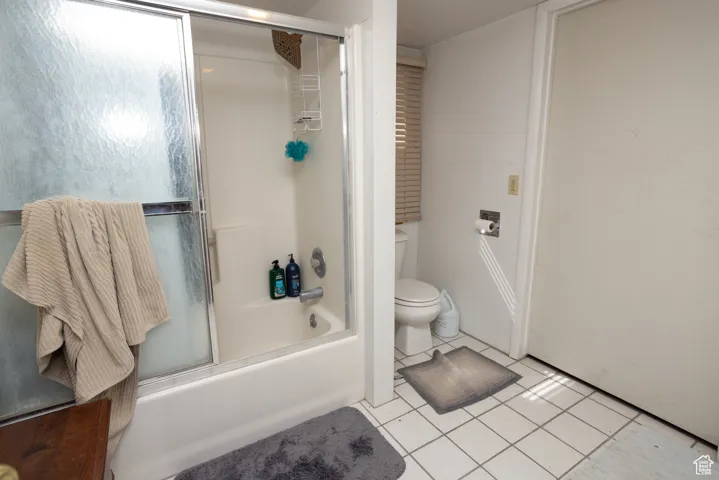 Bathroom with tile patterned floors, shower / bath combination with glass door, and toilet