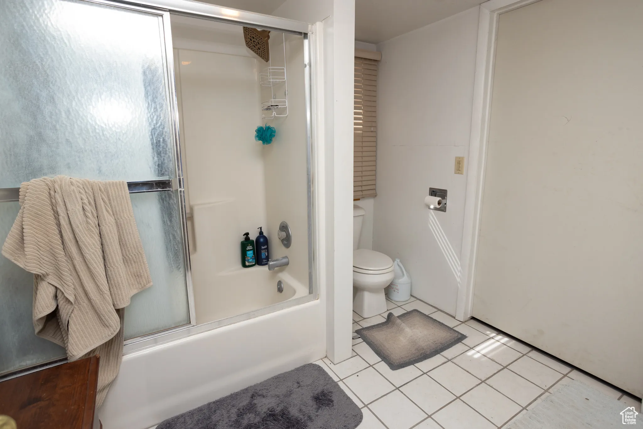 Bathroom with tile patterned flooring, enclosed tub / shower combo, and toilet