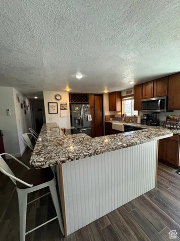 Kitchen featuring refrigerator with ice dispenser, a kitchen breakfast bar, sink, and stone counters