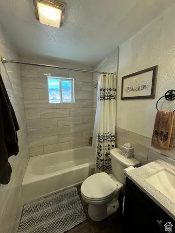 Full bathroom featuring shower / bath combo with shower curtain, vanity, toilet, and a textured ceiling
