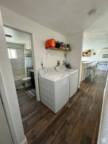 Laundry area with dark wood-type flooring, independent washer and dryer, and a textured ceiling