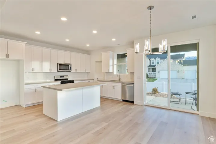 Kitchen with decorative light fixtures, white cabinets, a center island, stainless steel appliances, and a healthy amount of sunlight