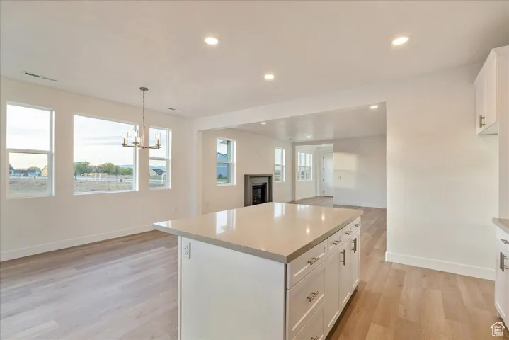 Kitchen featuring white cabinetry, decorative light fixtures, a center island, and a healthy amount of sunlight