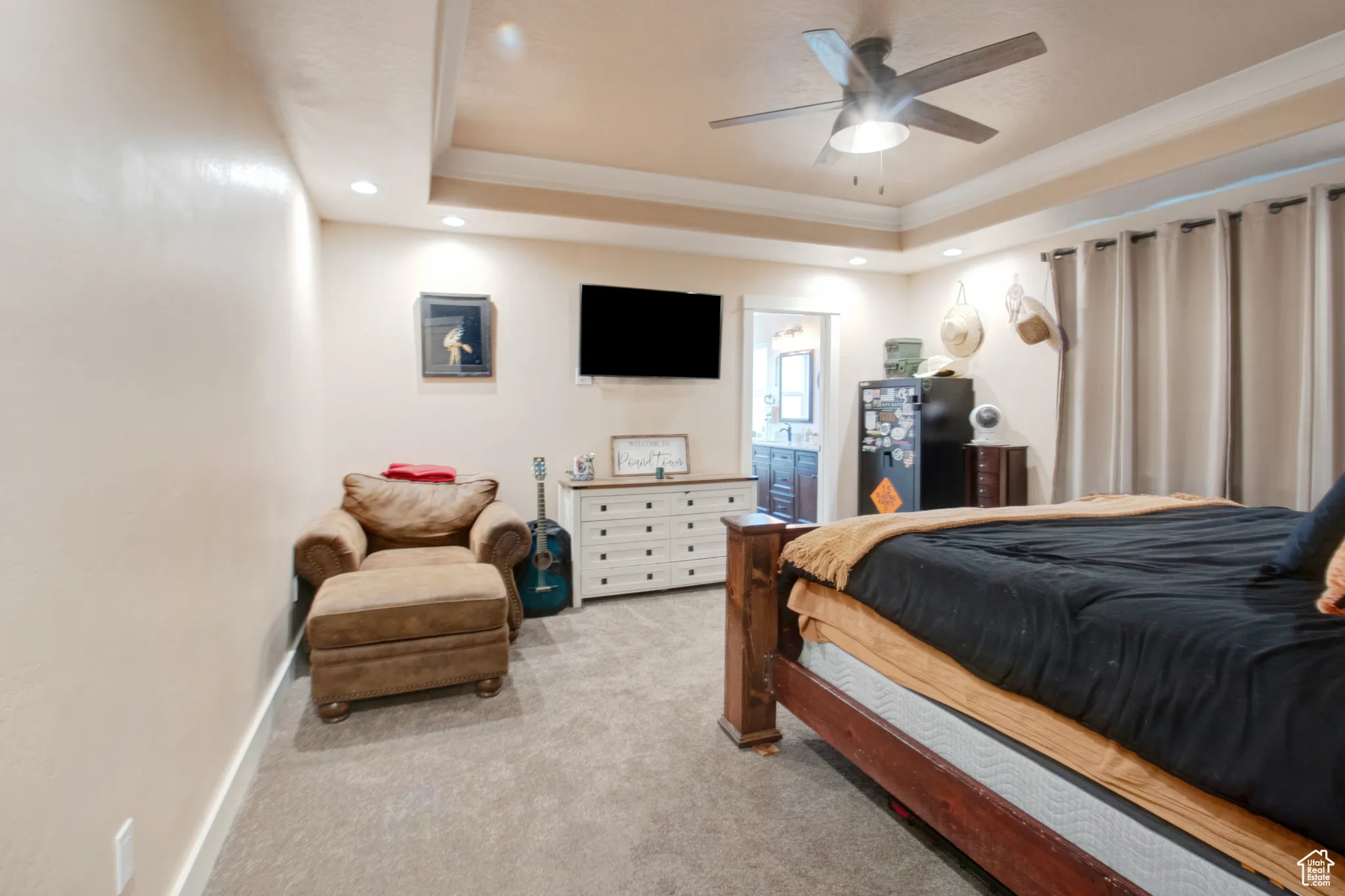 Bedroom with ensuite bath, ornamental molding, a raised ceiling, and light carpet