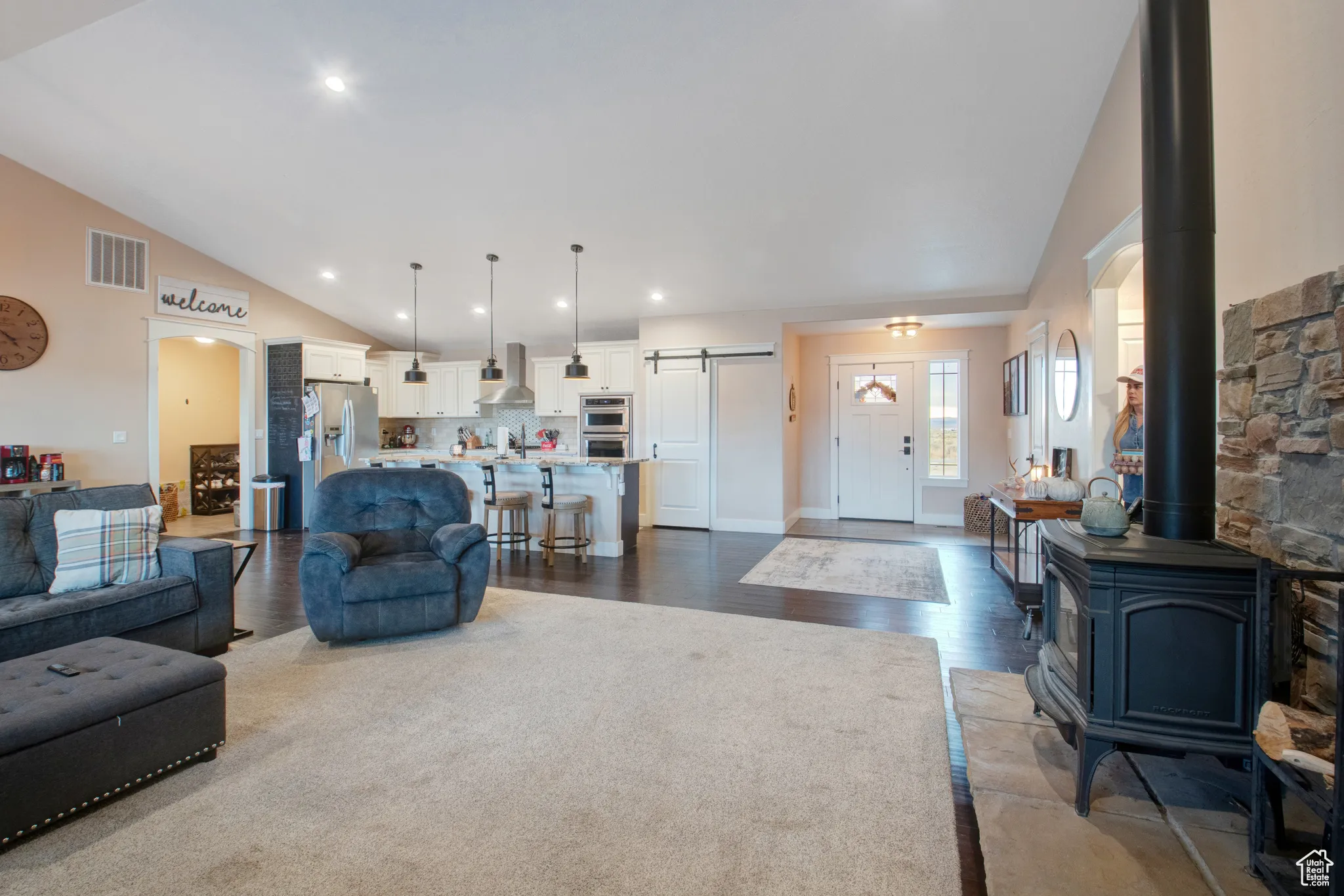Living room featuring high vaulted ceiling, a barn door, hardwood / wood-style floors, and a wood stove