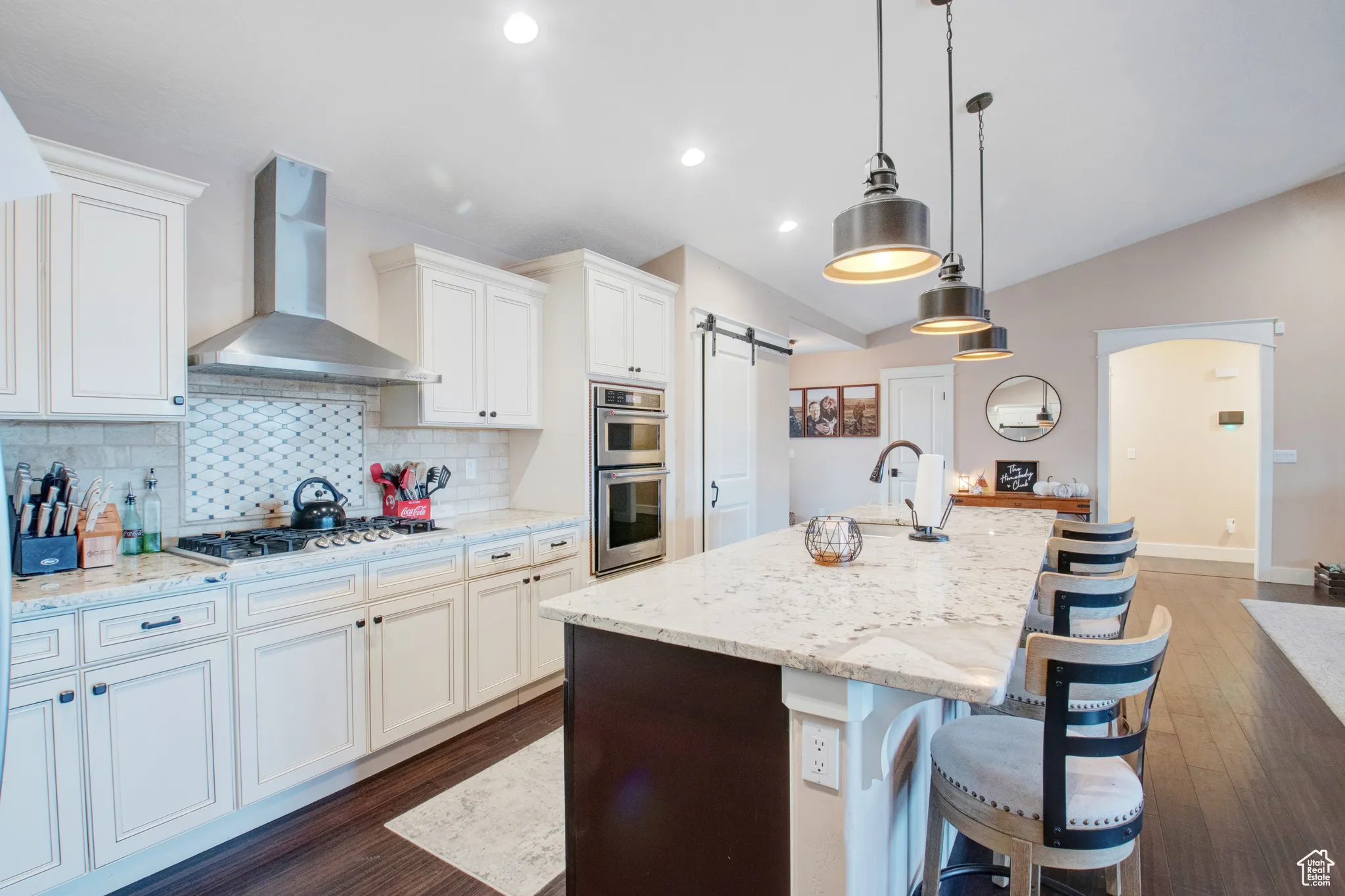Kitchen with a kitchen island with sink, a barn door, wall chimney exhaust hood, and appliances with stainless steel finishes