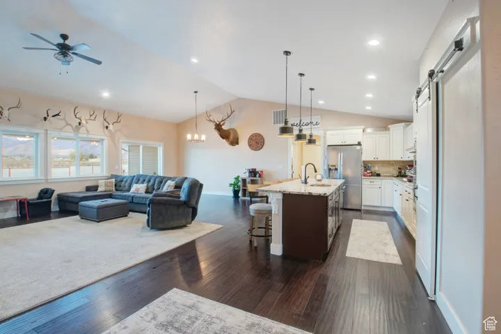 Kitchen featuring a breakfast bar, stainless steel fridge with ice dispenser, a center island with sink, pendant lighting, and white cabinets