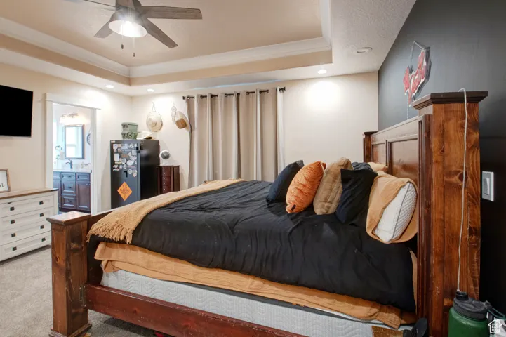 Bedroom with connected bathroom, ornamental molding, light colored carpet, and a raised ceiling