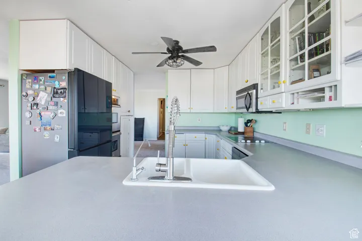 Kitchen featuring sink, refrigerator, black electric cooktop, ceiling fan, and white cabinets
