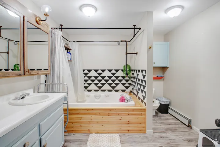 Full bathroom featuring hardwood / wood-style floors, a baseboard radiator, vanity, toilet, and shower / bath combo