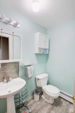 Bathroom with a baseboard heating unit, hardwood / wood-style floors, sink, and toilet