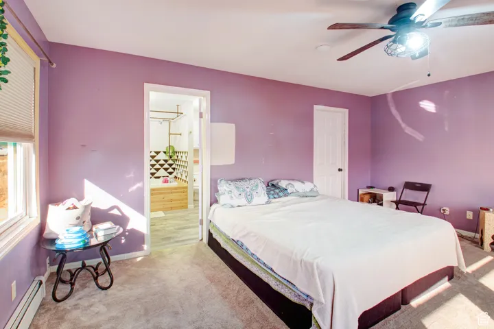 Bedroom featuring ceiling fan, a baseboard radiator, ensuite bathroom, and light colored carpet