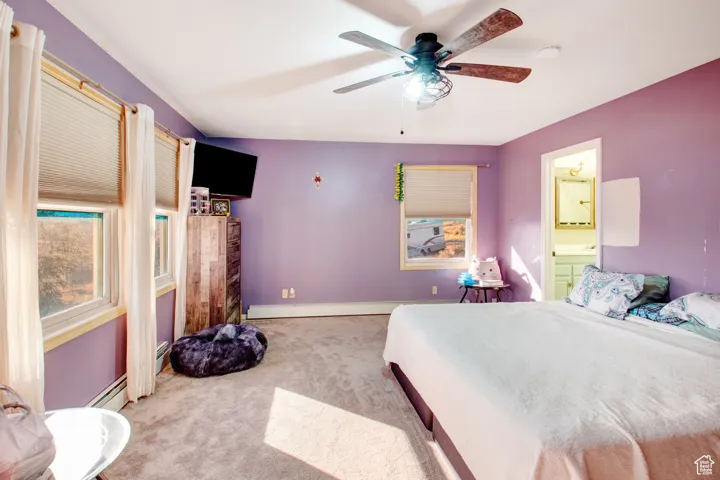 Carpeted bedroom featuring ceiling fan, a baseboard radiator, and connected bathroom