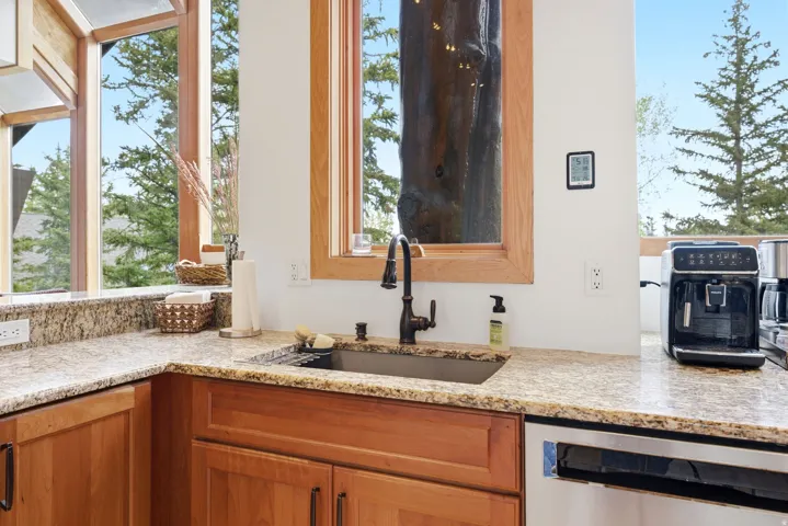 Kitchen featuring granite countertops, wood cabinetry, an undermount sink with a dark-finish faucet, and a stainless steel dishwasher