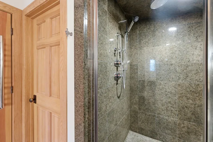 Walk-in shower featuring tiled walls, glass enclosure, and a chrome multi-function showerhead system
