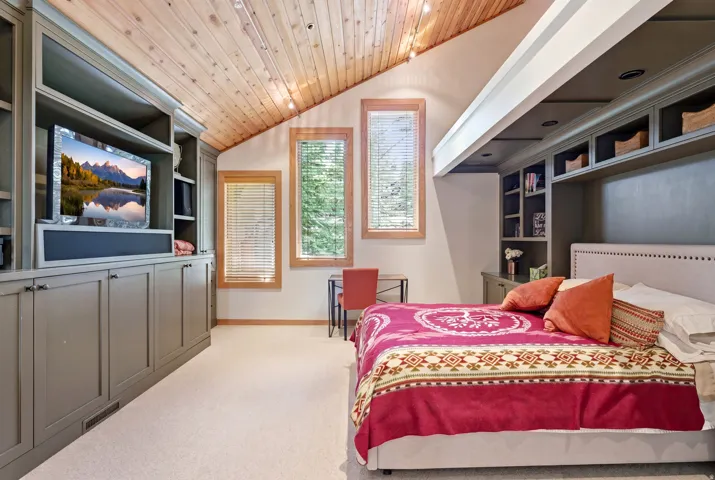Room featuring a sloped wood-paneled ceiling with recessed lighting, two vertical windows with blinds, built-in cabinetry with open shelving and closed storage, and light-colored carpeting