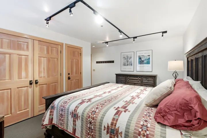 Bright room featuring a dark wood bed frame, track lighting, light wood paneled doors, and a dark wood dresser