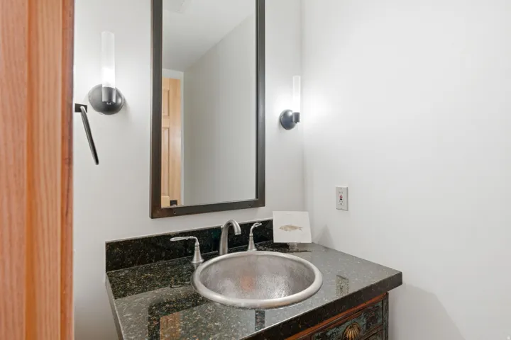 Vanity featuring a dark stone countertop, an oval vessel sink with a brushed metal finish, and a coordinating two-handle faucet