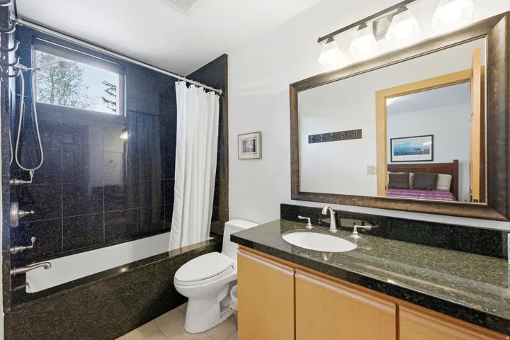 Bathroom featuring a bathtub with dark tile surround, a built-in window, a single vanity with stone countertop, and light wood cabinetry
