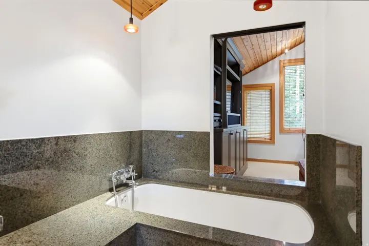 Built-in soaking tub with dark speckled stone surround and polished chrome fixtures