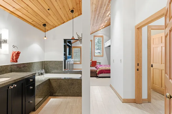 Vaulted wood-paneled ceiling, integrated bathtub, stone-finish countertops, wood-finish flooring, and natural wood trim throughout