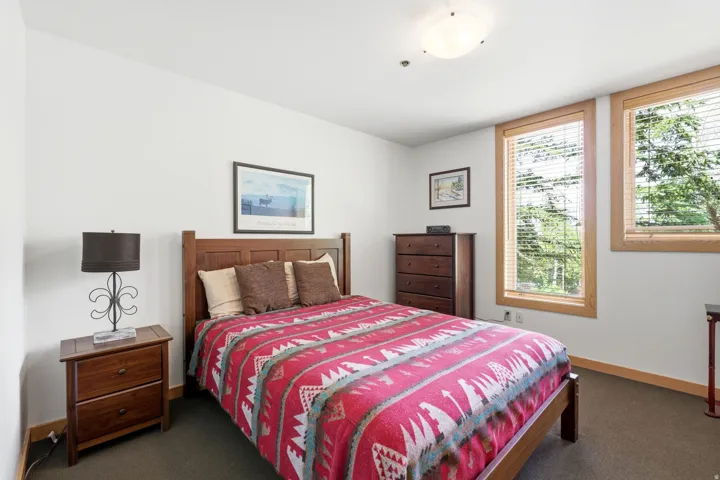 Carpeted bedroom featuring two large windows with natural wood trim and blinds