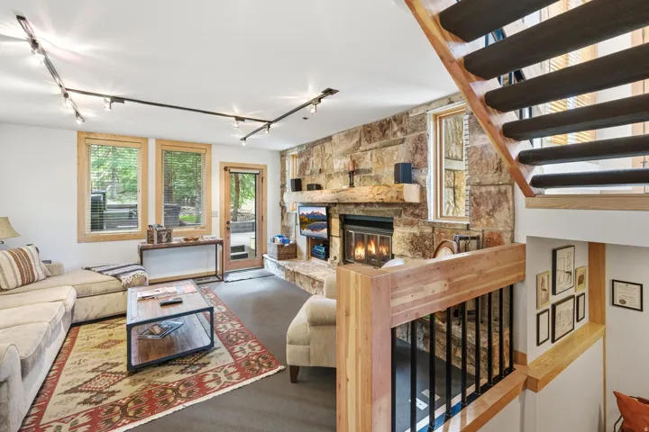 Open-concept living area featuring a stone fireplace with a wood mantle, wood-frame windows, and a glass-panel door providing outdoor access