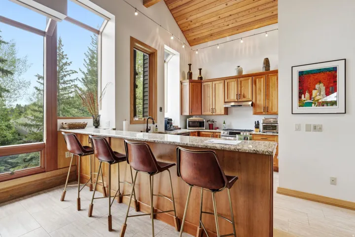 Kitchen featuring a vaulted wood-paneled ceiling with track lighting, wood cabinetry, built-in stainless steel range hood, and a light-toned countertop island with seating