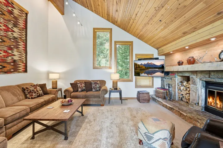 Spacious room featuring a vaulted wood-paneled ceiling, a stone fireplace with a wood-burning insert, and multiple windows