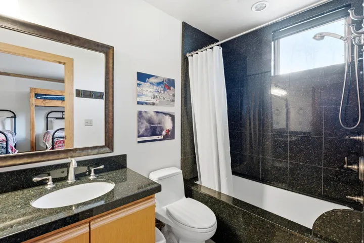 Bathroom featuring a granite countertop vanity with a rectangular undermount sink, a framed mirror, and a bathtub with a granite tile surround