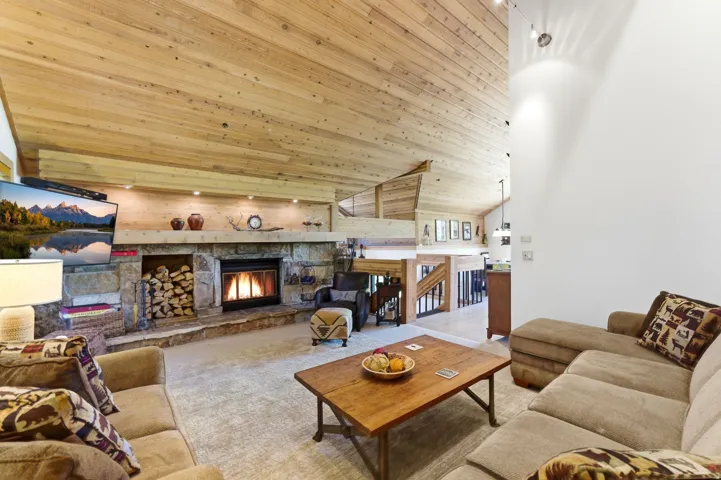Living area featuring a natural wood-plank ceiling, a stone fireplace with a raised hearth, and built-in wood storage