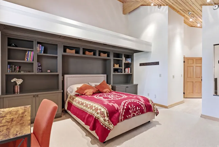 Bedroom featuring a built-in wall unit with shelving and cabinetry, a padded headboard, a vaulted wood-finish ceiling, and light-toned flooring