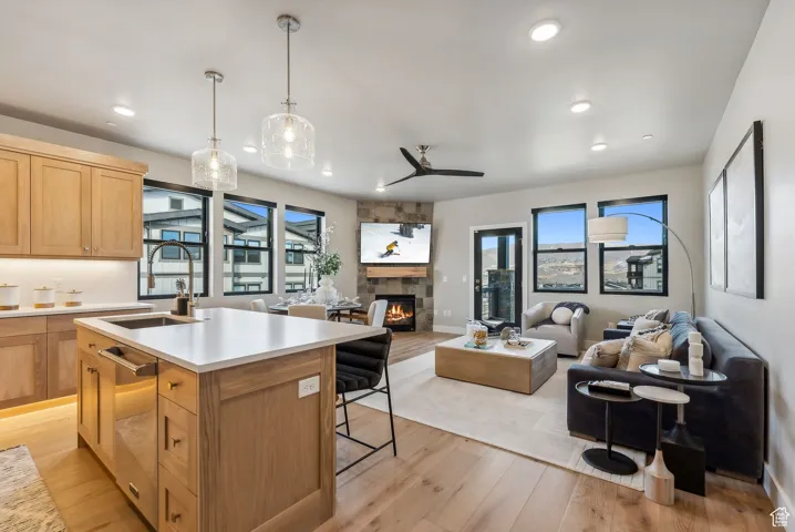 Kitchen with sink, decorative light fixtures, a center island with sink, light wood-type flooring, and a fireplace