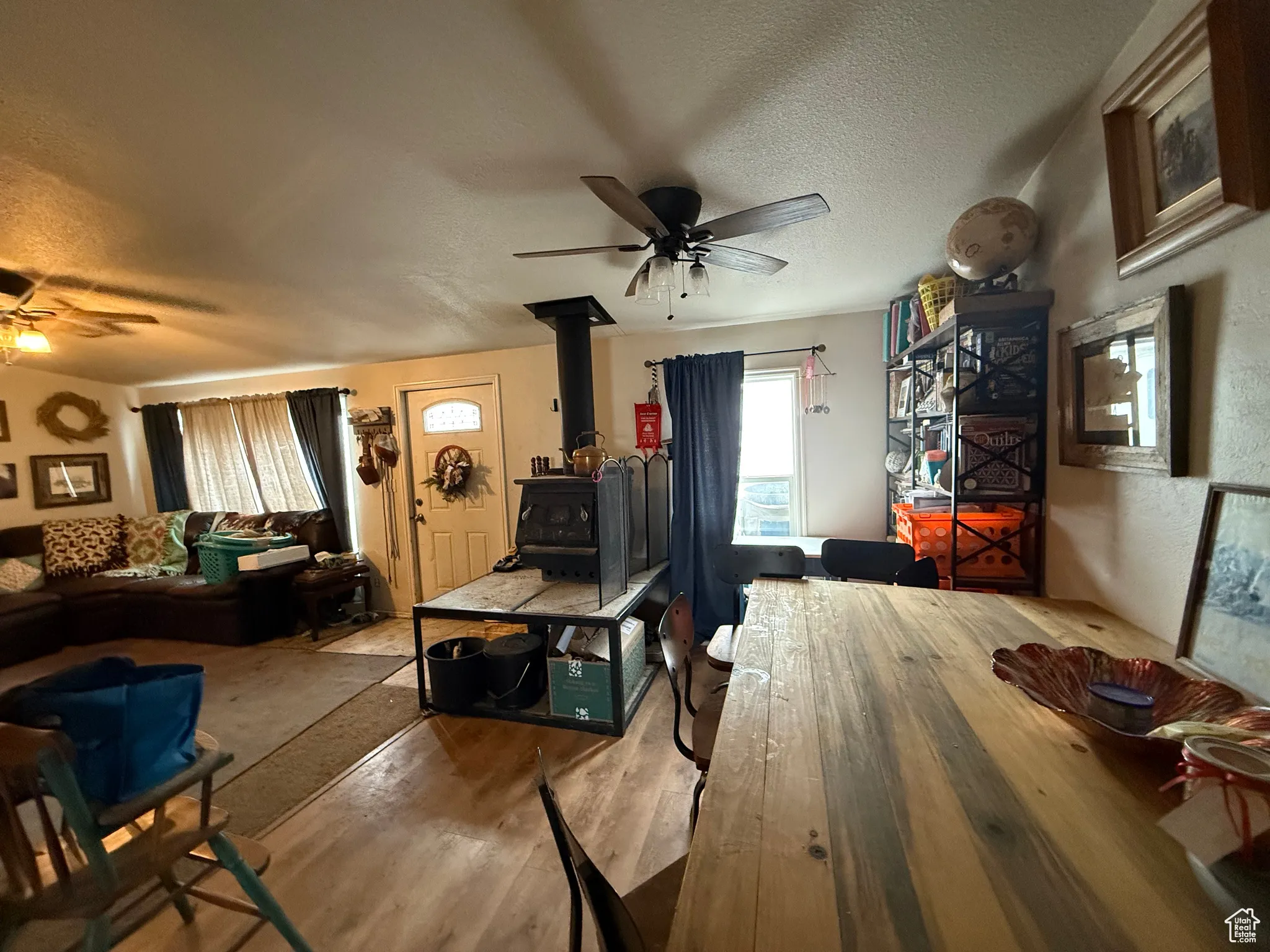 Dining space featuring ceiling fan, light hardwood / wood-style floors, a textured ceiling, and a wood stove