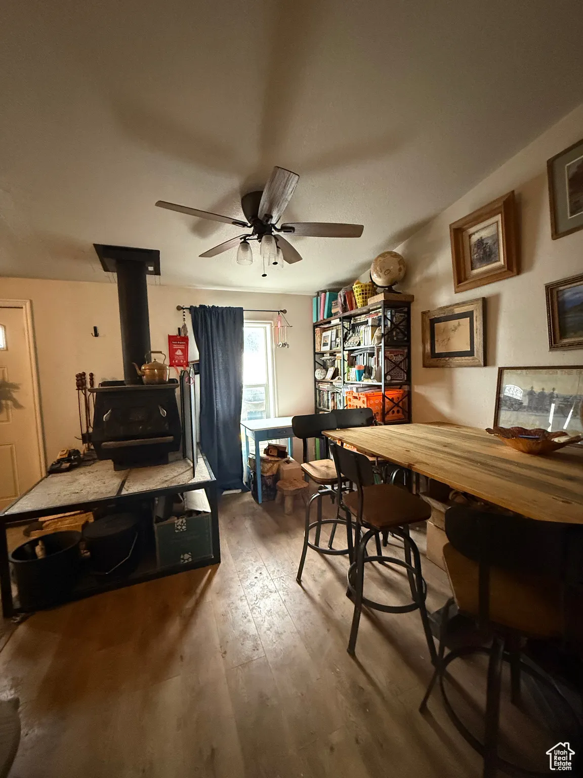 Dining area with wood-type flooring, a wood stove, and ceiling fan