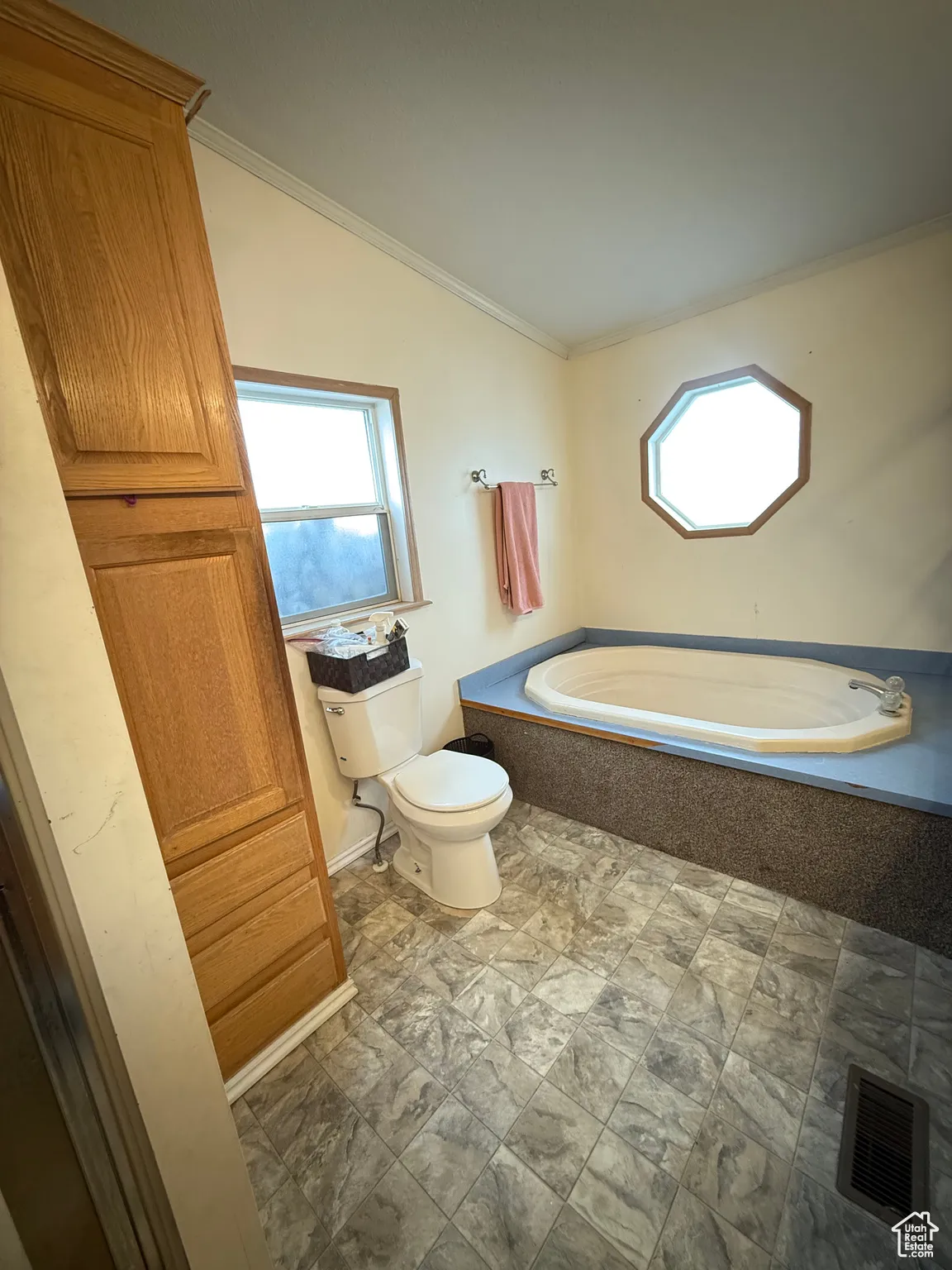 Bathroom with a relaxing tiled tub, ornamental molding, lofted ceiling, and toilet