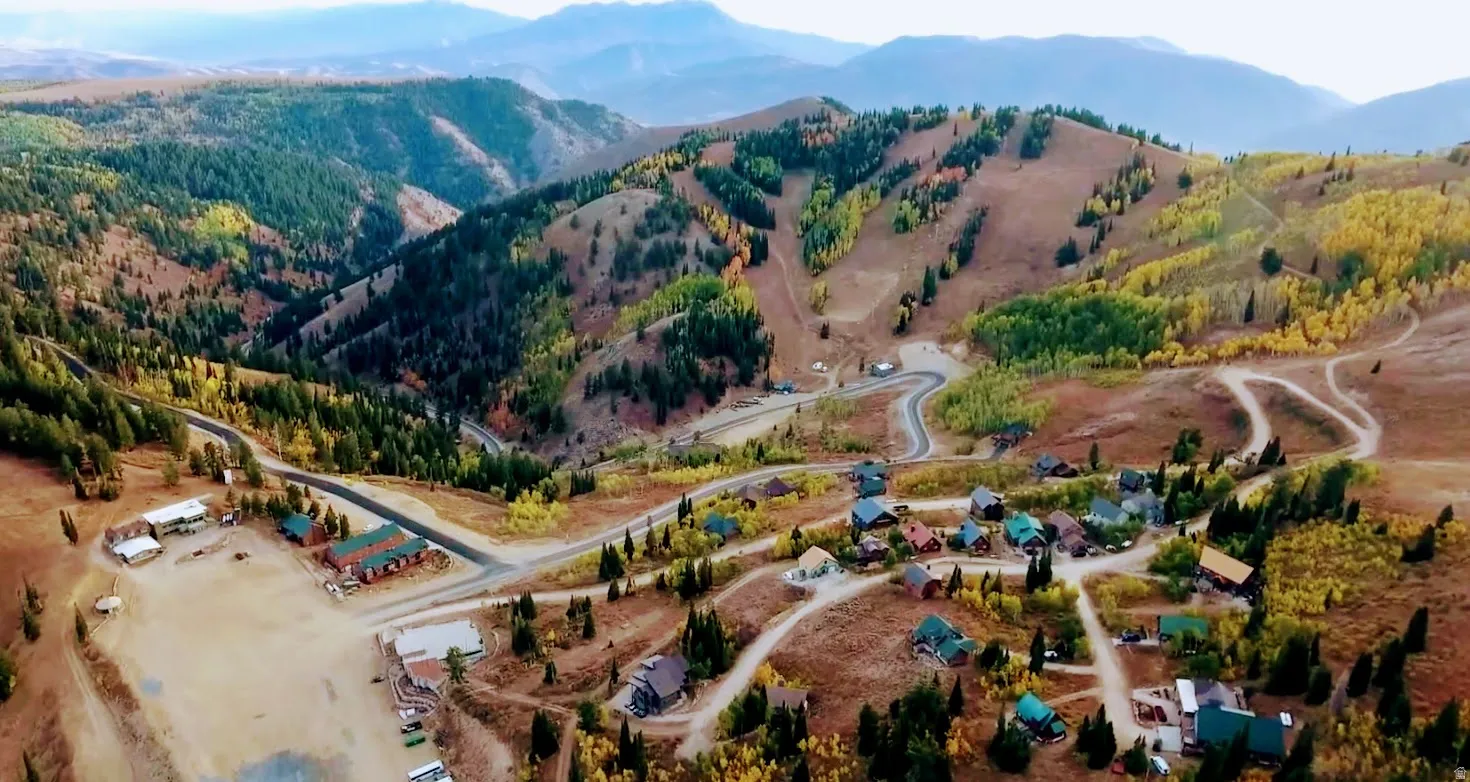 Mountainous terrain featuring a village of structures, winding roads, and extensive tree coverage including golden foliage