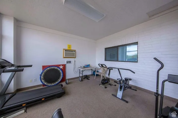 Workout room featuring a textured ceiling, a wall mounted AC, baseboards, and carpet