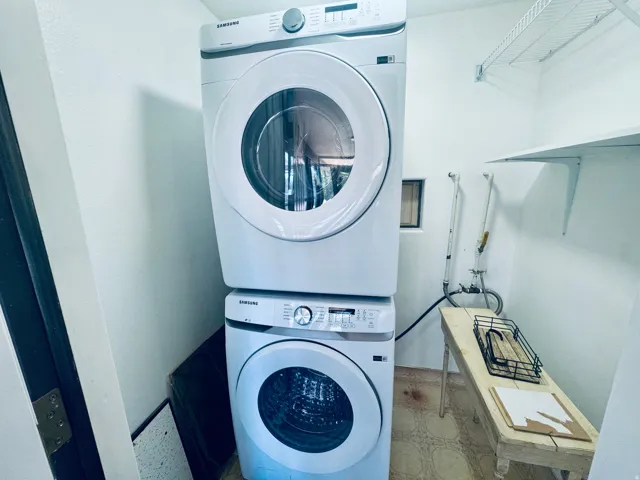Dedicated laundry area with stackable washer and dryer appliances, wall-mounted shelving, and a small utility window