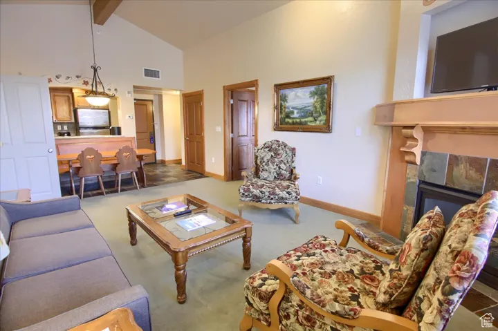 Carpeted living room with high vaulted ceiling, a tile fireplace, and beamed ceiling